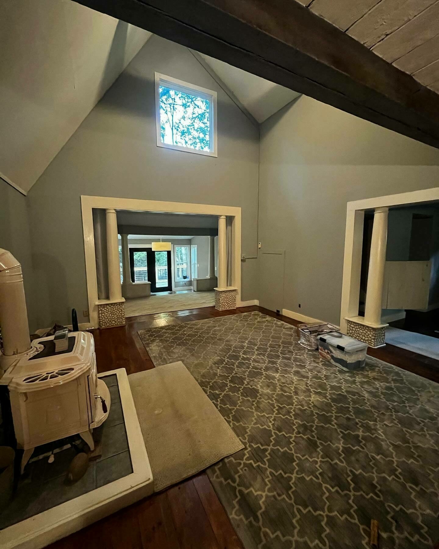 An empty room with high ceilings, a patterned rug, and construction materials scattered, suggesting ongoing renovation work within a residential space.
