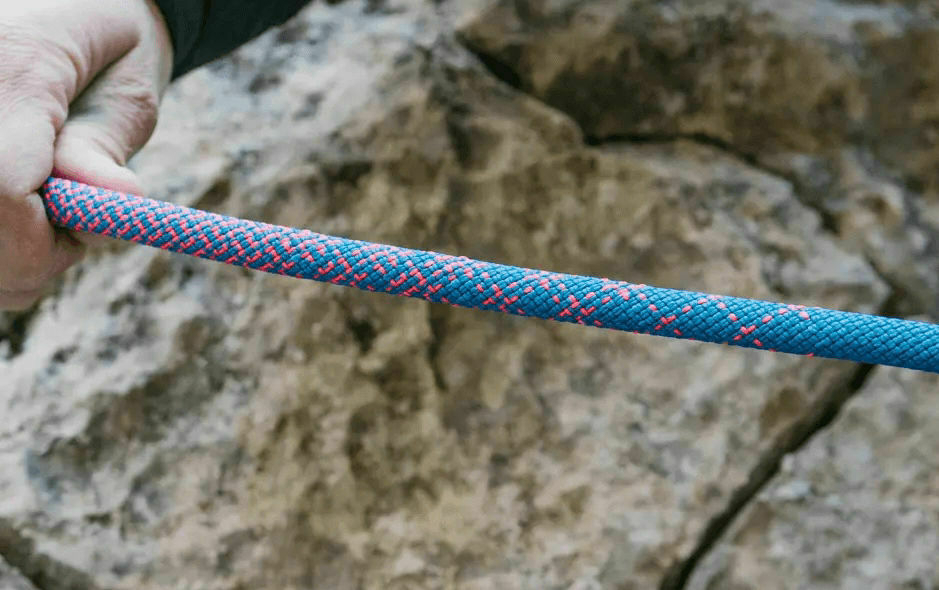 A hand grips a blue and red climbing rope against a rocky backdrop.