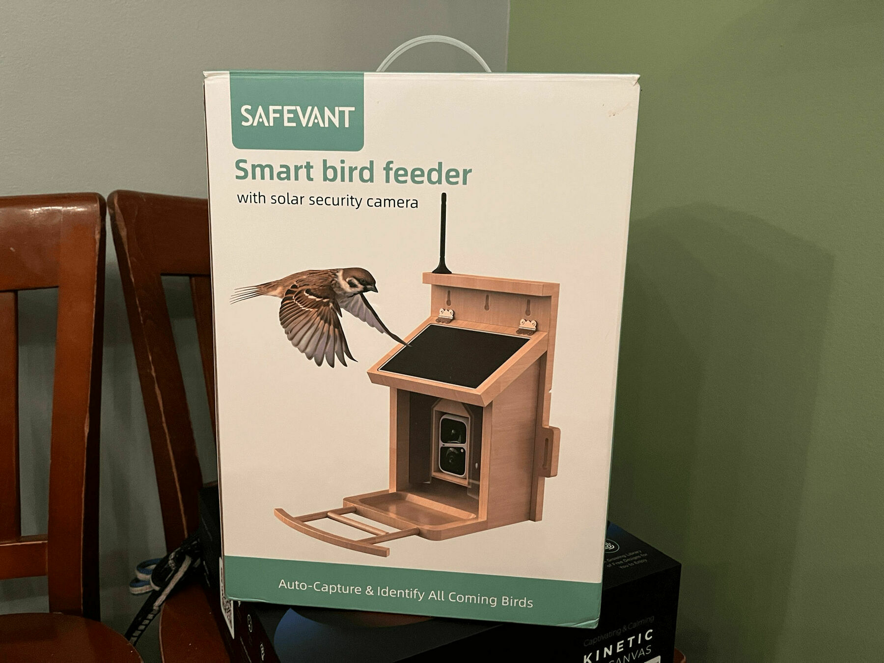 A package featuring a “Smart bird feeder with solar security camera” sits atop a table. It claims to “Auto-Capture & Identify All Coming Birds.” An illustrated bird is approaching the feeder.